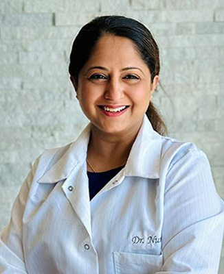 The image shows a woman wearing a white lab coat, posing for the camera with a smile.