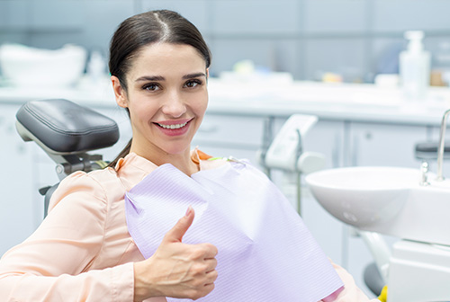 A woman in a dental office, smiling and giving a thumbs-up while sitting in the dentist s chair.