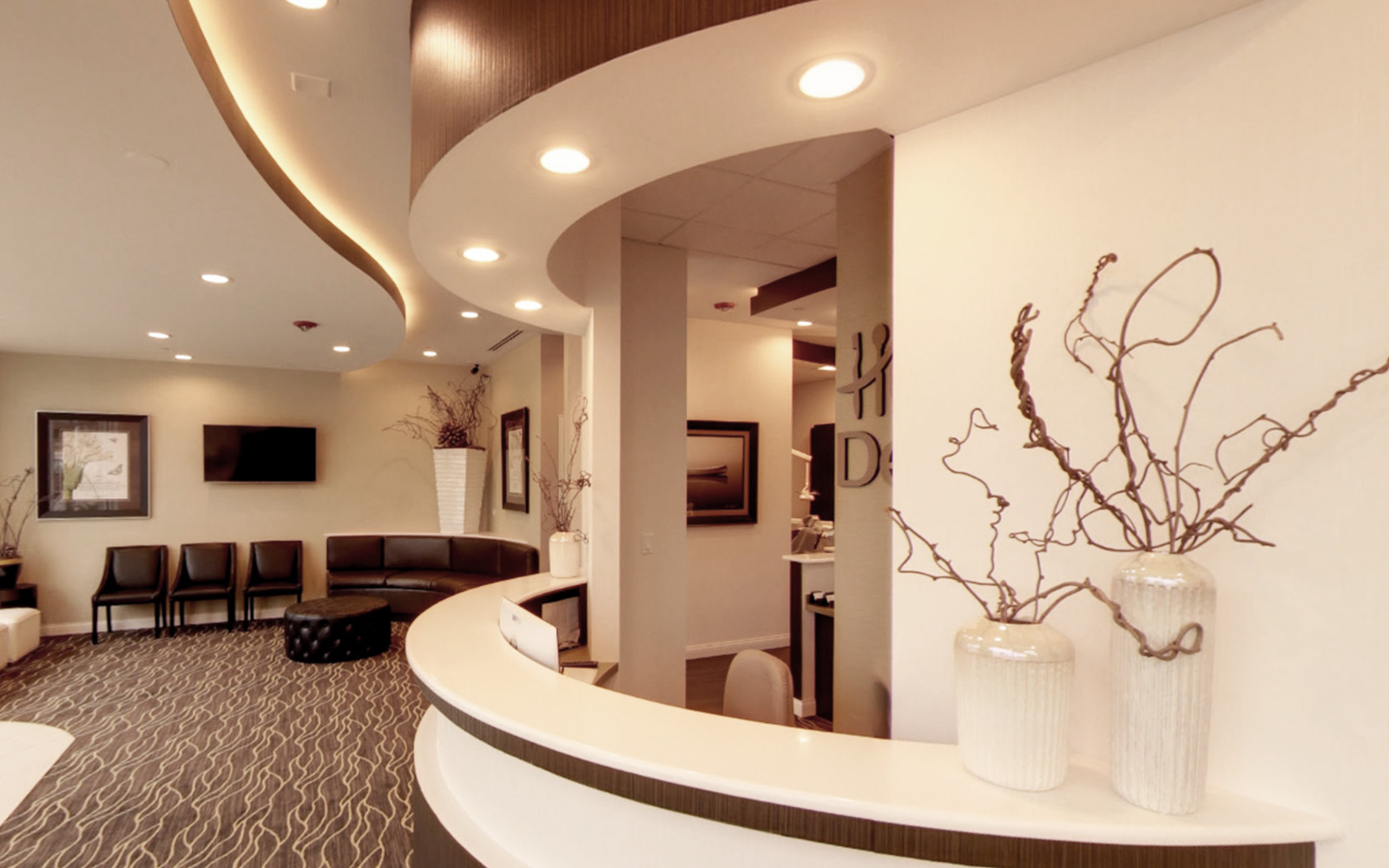 The image depicts an interior space, likely a lobby or waiting area, featuring modern decor with a curved countertop, seating arrangement, and wall art.