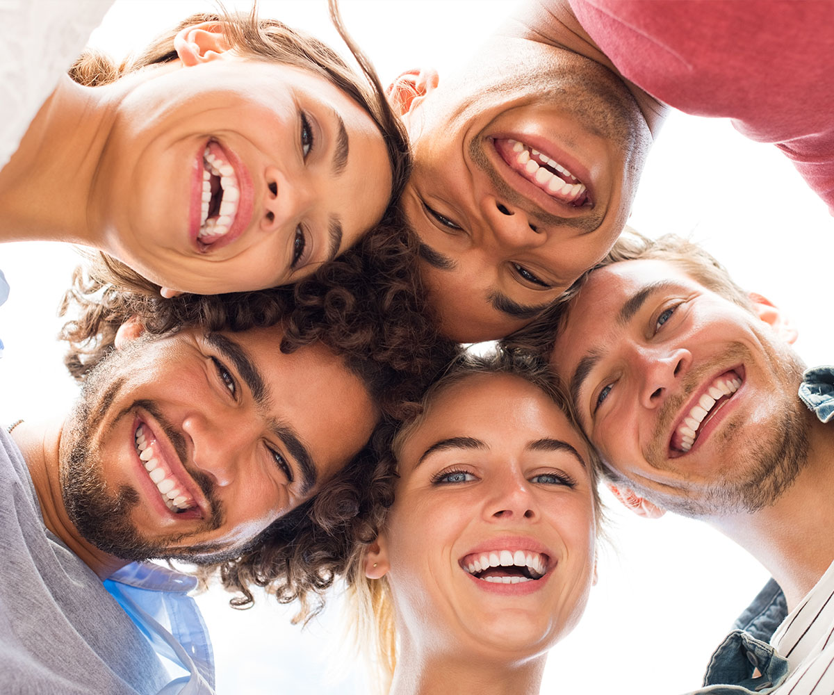 The image shows a group of six young adults with radiant smiles, posing closely together, seemingly celebrating or enjoying a moment of happiness.